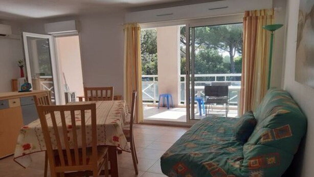 A room with a dining table and chairs, a sofa, a sliding glass door leading to an outdoor area, and a small kitchen area. - Apartment for 4, air-conditioned 4, Terrace 15 m² - beach, town center on foot (Mandelieu-la-Napoule)