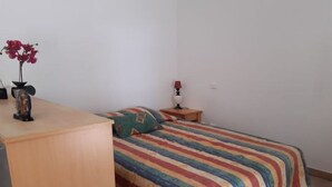 A bedroom with a bed, a nightstand, a lamp, and a small table with a vase of flowers. - Apartment for 4, air-conditioned 4, Terrace 15 m² - beach, town center on foot (Mandelieu-la-Napoule)