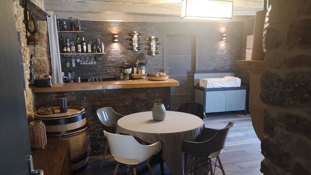 Eine rustikale Bar mit Steinwand, Holzbottichen und einem runden Tisch mit Stühlen.