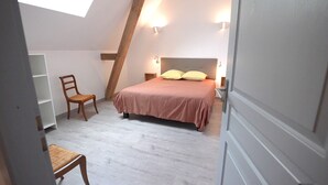 Una camera da letto con soffitto spiovente, un letto con due cuscini, una sedia e un comodino.