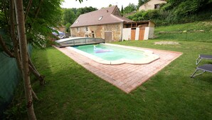 Un giardino con piscina, un portico coperto e una casa in pietra.