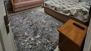 Una habitación pequeña y poco amueblada con una cama, un sofá, una mesita de madera y una alfombra.