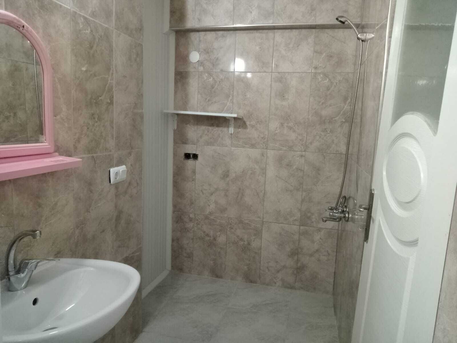 A bathroom with a sink, mirror, shower, and a door.