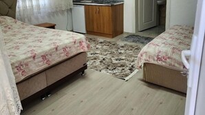 Una habitación pequeña y bien iluminada con dos camas, una kitchenette y un baño.