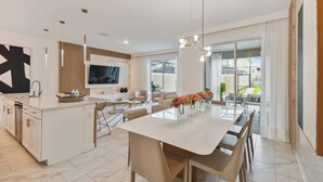 Une cuisine moderne dotée d’un îlot central, un coin repas avec une longue table et un espace de vie comprenant un téléviseur et des sièges.