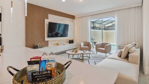 Un salon moderne avec un téléviseur, un canapé et une table basse. Un panier de bienvenue contenant des articles de toilette est posé sur la table.