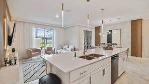 Une cuisine moderne dotée d’un grand îlot central, de meubles blancs et d’un éclairage suspendu.