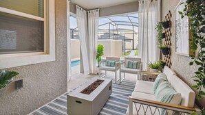 Un salon moderne avec un canapé blanc, une table basse et une cheminée. On y trouve des plantes en pot et une vue sur une piscine.