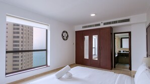 A hotel room with a large window, a bed with white linens, a wooden wardrobe, and a bathroom visible through an open door.