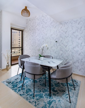 A dining area with a marble table, four grey chairs, a blue patterned rug, and a wall with a leaf pattern. - Spacious 2 bedroom with Amazing Marina View Rimal JBR (Dubai)