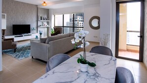 A modern living room with a sofa, TV, and a dining area with a marble table and chairs.