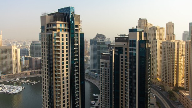 A high-rise building with a modern design, surrounded by a marina and a busy road.