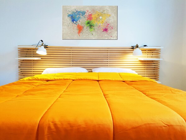Un dormitorio con cabecera de madera, una colcha anaranjada grande, dos lámparas de noche y un cuadro abstracto colorido en la pared.