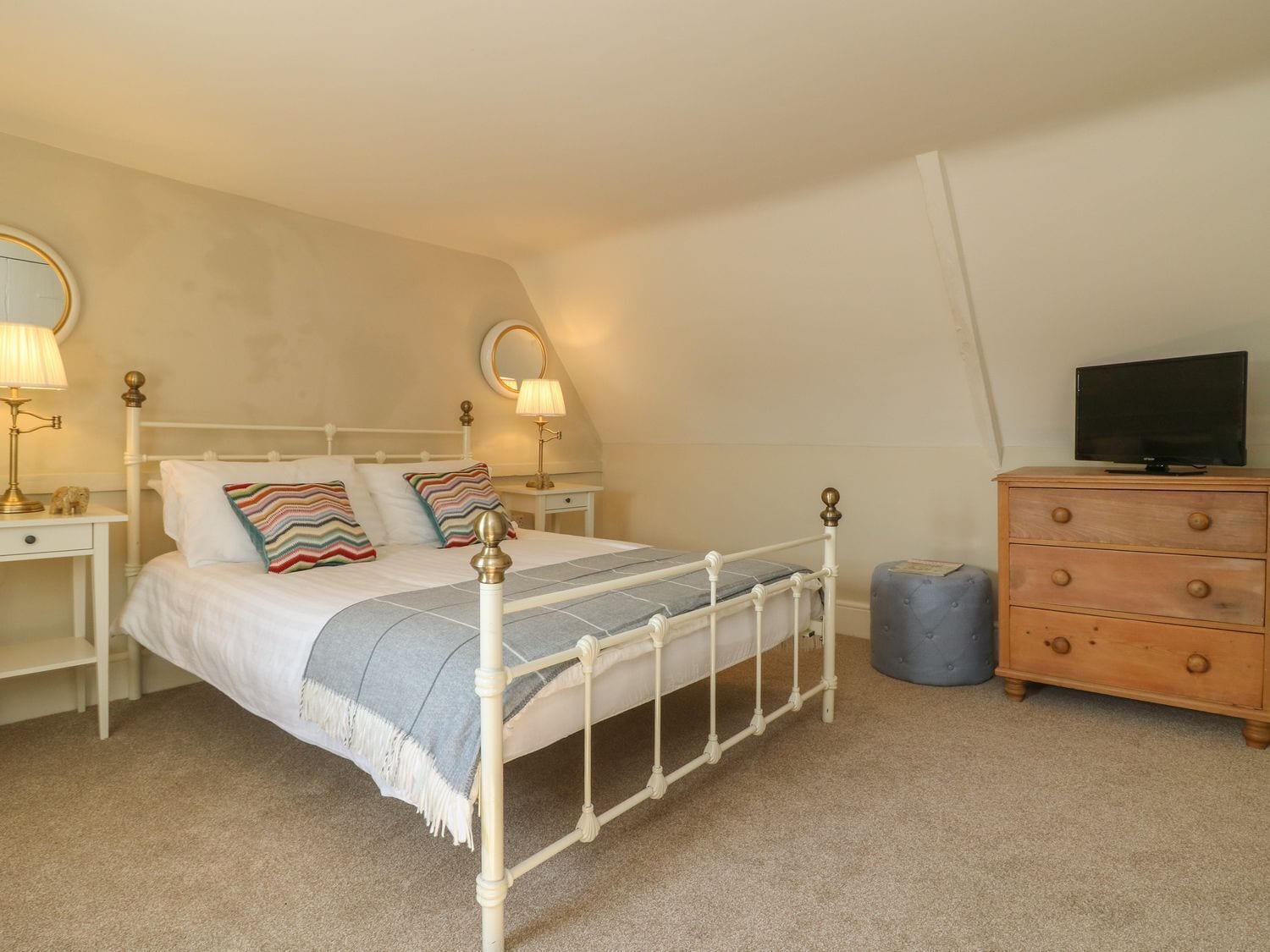 A neatly arranged bedroom with a bed, bedside tables, a dresser, and a television.