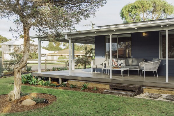 Une maison moderne dotée d’un patio couvert, aménagé avec du mobilier d’extérieur et une grande fenêtre.