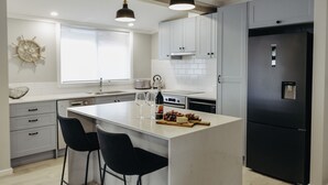 Een moderne keuken met witte kasten, een centraal eiland met barkrukken, een zwarte koelkast en hanglampen.