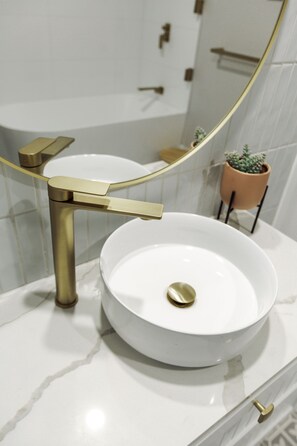 Une salle de bain avec un lavabo blanc, un robinet doré et une plante en pot.