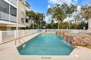A swimming pool with a '3 1/2 NO DIVING' sign, surrounded by a white fence, palm trees, and a multi-story building with balconies. - Shadowbrooke - 3 bed/2 bath - Monthly Rentals (St. Simons Island)