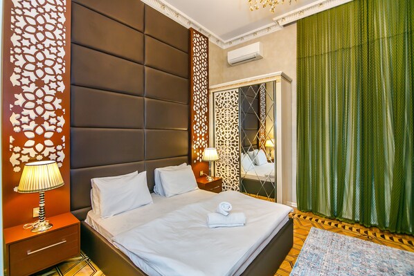 A hotel room with a large bed, a nightstand with a lamp, a mirror, and green curtains.