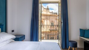 Une chambre d’hôtel avec un balcon, un lit, une table de chevet et un petit coin salon.