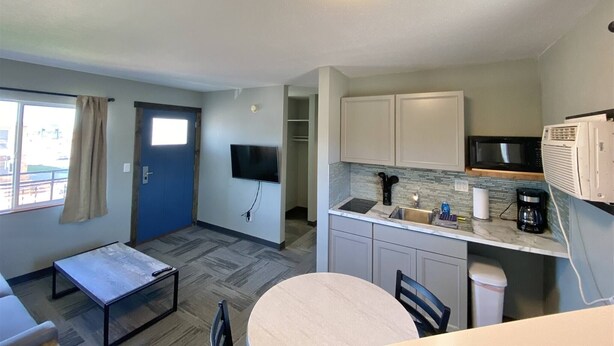Habitación de hotel compacta con kitchenette, zona de comedor, televisor y ventana con cortinas.