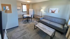 Un espacio habitable compacto con sofá, una mesita, una mesa de comedor con sillas, un refrigerador y una ventana con cortinas.