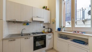 Eine moderne Küche mit hellen Holzschränken, einem Gasherd, einer Spüle und einem Fenster mit Blick auf einen Balkon.