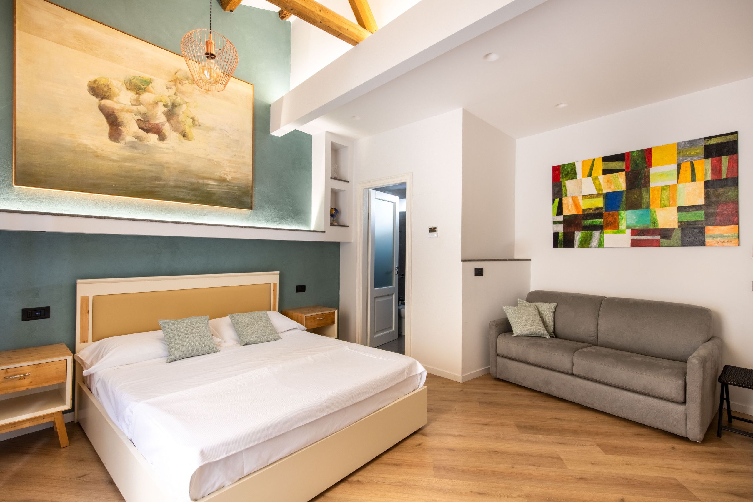 A modern bedroom with a large bed, a gray sofa, and two paintings on the walls.