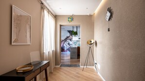 Un couloir doté d’un plancher en bois, un bureau avec un plateau, une œuvre d’art encadrée, une horloge murale et une porte donnant sur une autre pièce.