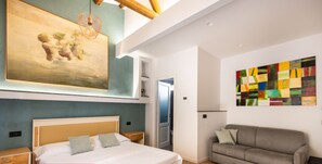 Ein modernes Schlafzimmer mit einem großen Bett, einem grauen Sofa und Kunstwerken an den Wänden.