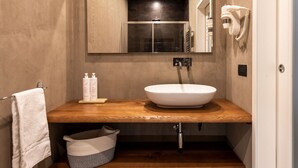 Ein Badezimmer mit einem Holzkosmetikschrank, einem weißen Waschbecken, einem Handtuchhalter, einem Haartrockner und einem Mülleimer.