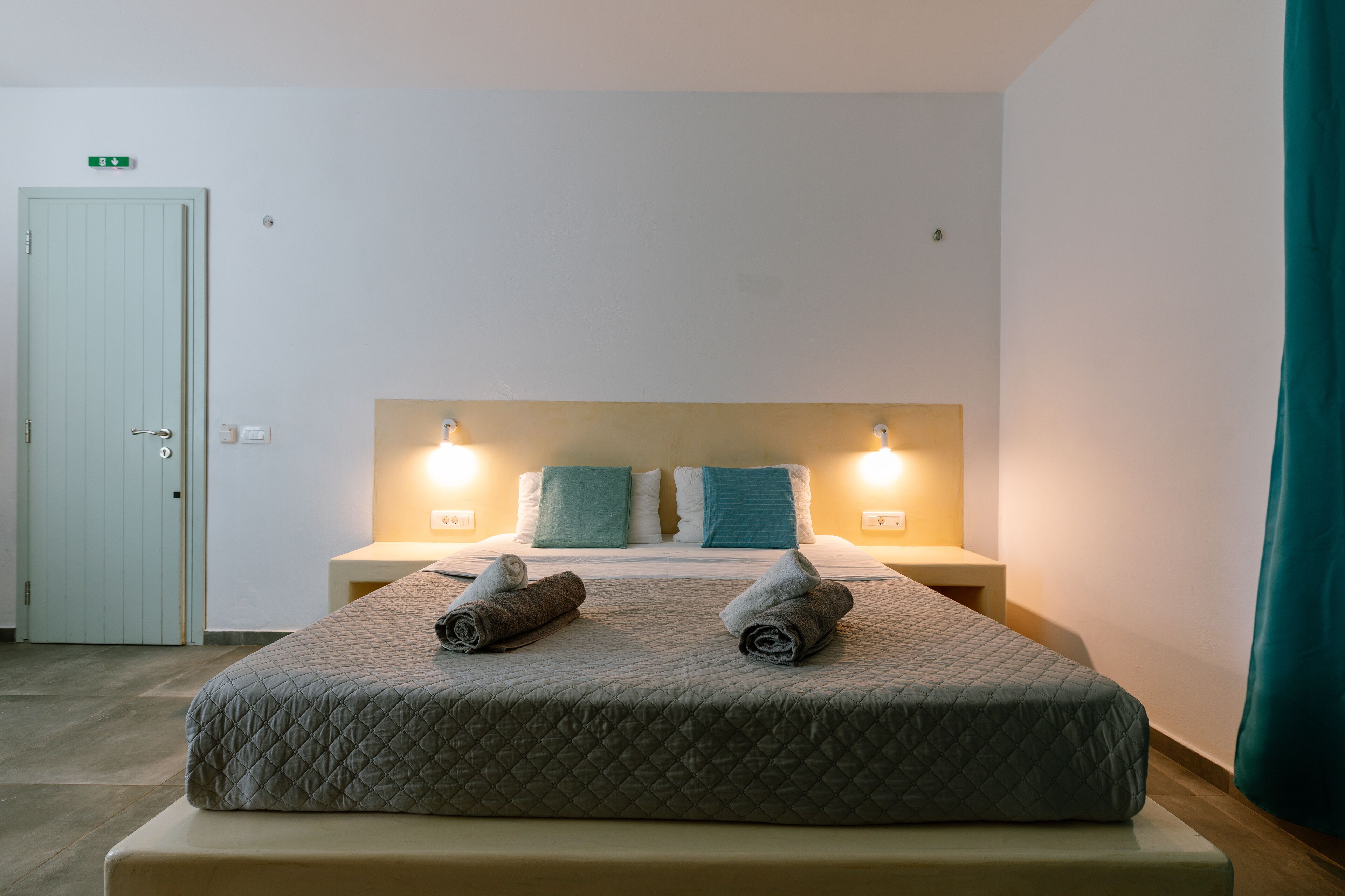 A hotel room with a bed, two bedside lamps, a door, and a green curtain.