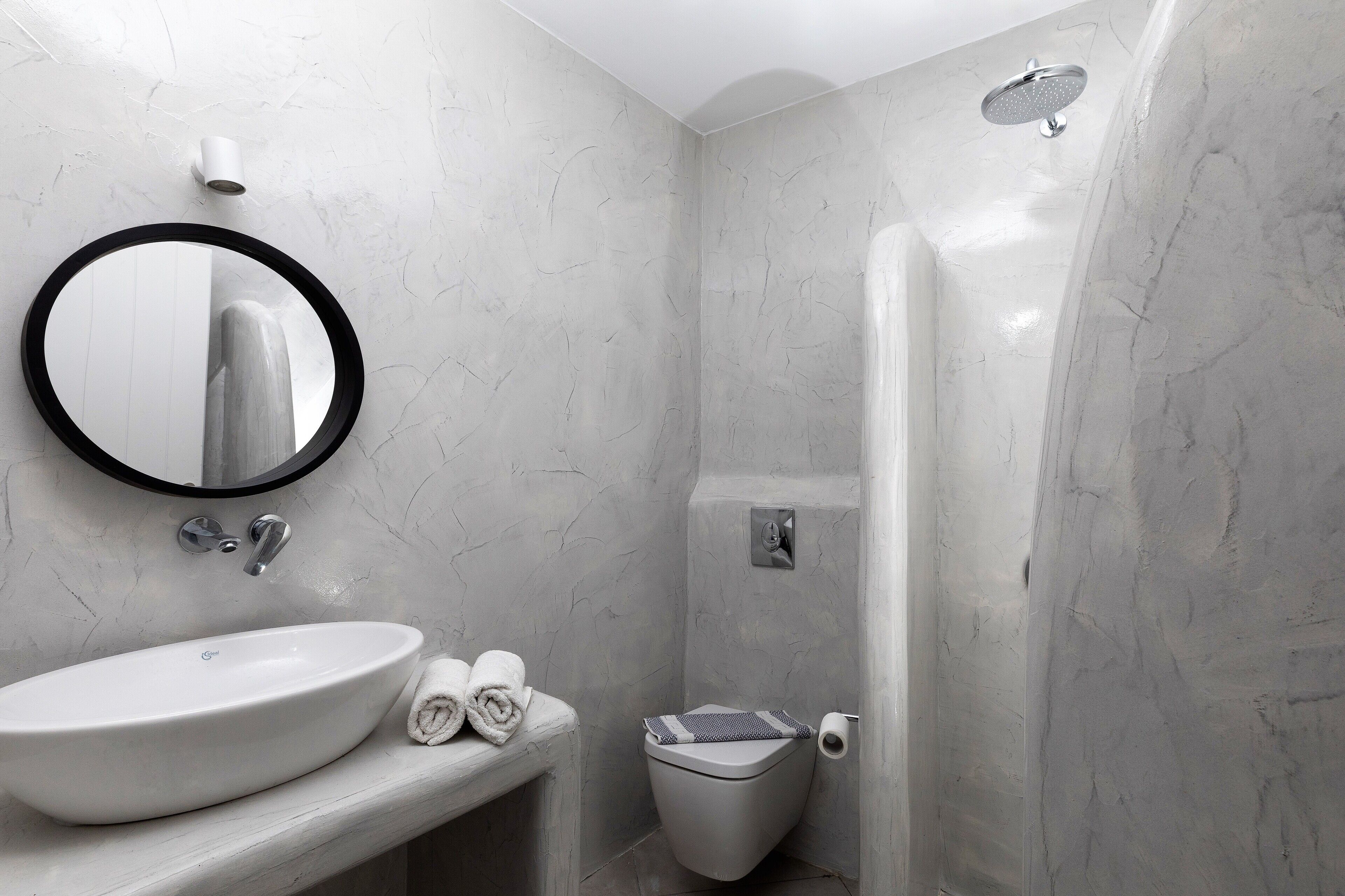 Une salle de bain avec un miroir rond, un lavabo, des toilettes et une douche.