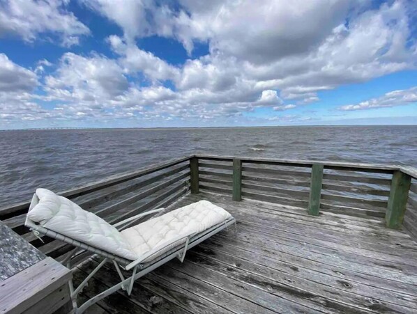 A wooden pier with a white cushioned lounge chair facing the sea.