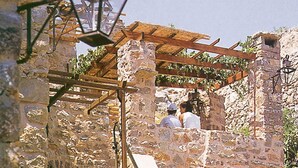 Een stenen gebouw met een houten trap, een houten pergola en een lantaarn.