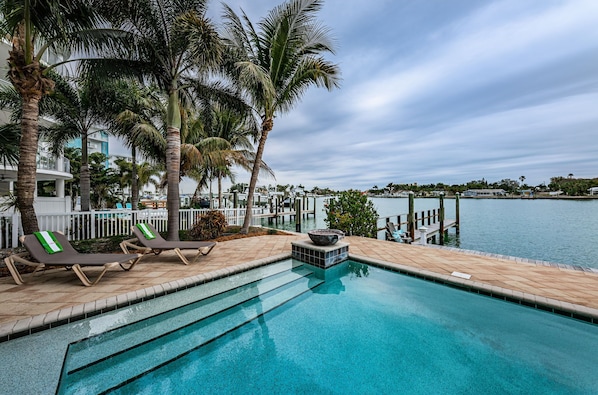 Relax by the tranquil pool overlooking the waterfront, surrounded by lush palm trees and a fire pit.
