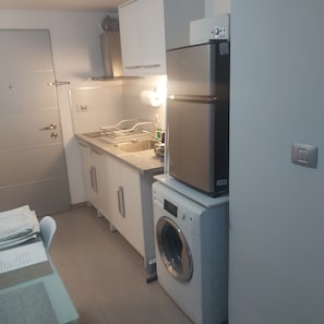 Een kleine keuken met een ingebouwde wasmachine, een spoelbak en keukenkastjes.