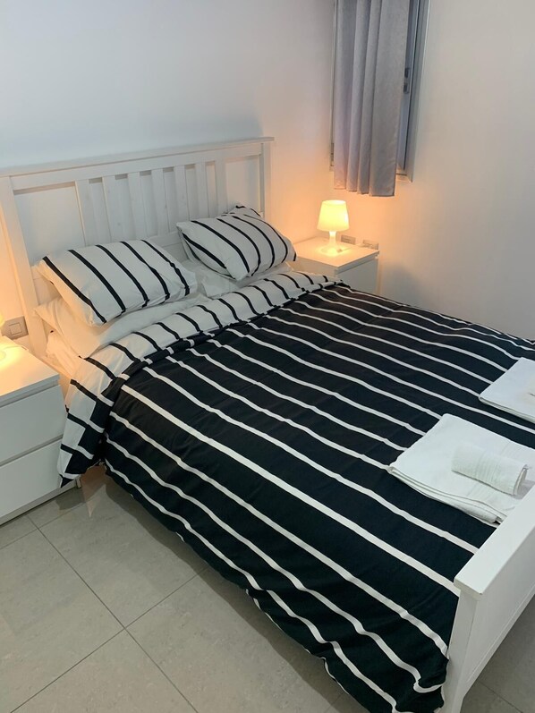 A neatly made bed with striped bedding, a bedside lamp, and a white nightstand.