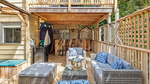 A covered outdoor seating area with wicker furniture, a wooden deck, and a view of the surrounding greenery. - Coastal Cottage, 4 Large Decks, Close to Beach, Short or Long Stays! (Blaine)