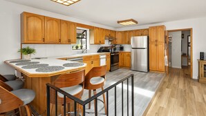 A modern kitchen with wooden cabinets, a stainless steel refrigerator, and a bar area with stools. - Coastal Cottage, 4 Large Decks, Close to Beach, Short or Long Stays! (Blaine)