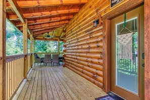 A log cabin with a wooden deck, a covered porch, and a window with a decorative screen.