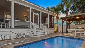 A swimming pool with a covered deck area, a patio with outdoor furniture, and a view of a residential building in the background. - Private Pool ~ Screened Porch ~ Pet Friendly (Destin)