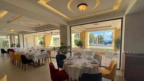A dining area with round tables set for service, large windows offering a view of the outdoors, and a modern ceiling design.