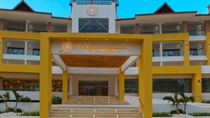 A hotel entrance with a yellow facade, multiple balconies, and a central entrance with steps leading up to it.
