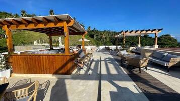 An outdoor seating area with wooden pergolas, wicker furniture, and a bar counter.