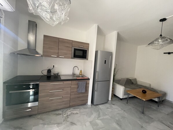 Eine moderne Küche mit Kühlschrank, Mikrowelle und Herd aus Edelstahl. Ein Holzunterschrank beherbergt ein Spülbecken, und ein kleiner Tisch trägt eine Schüssel.