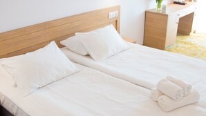 A neatly made bed with white linens and pillows, a wooden headboard, and a small bedside table with a vase of flowers. - Hotel Amber Port (Darlowo)