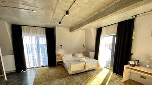 A hotel room with a large bed, a desk with a coffee maker, and a view of the city through the window. - Hotel Amber Port (Darlowo)