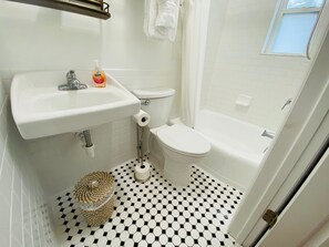 A bathroom with a white sink, toilet, and bathtub. There is a patterned floor and a window with a view.