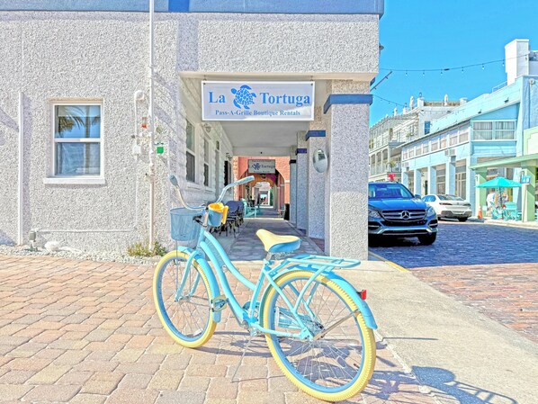 A turquoise bicycle parked in front of a building with a sign reading "La Tortuga Pass-A-Grille Boutique Rentals".